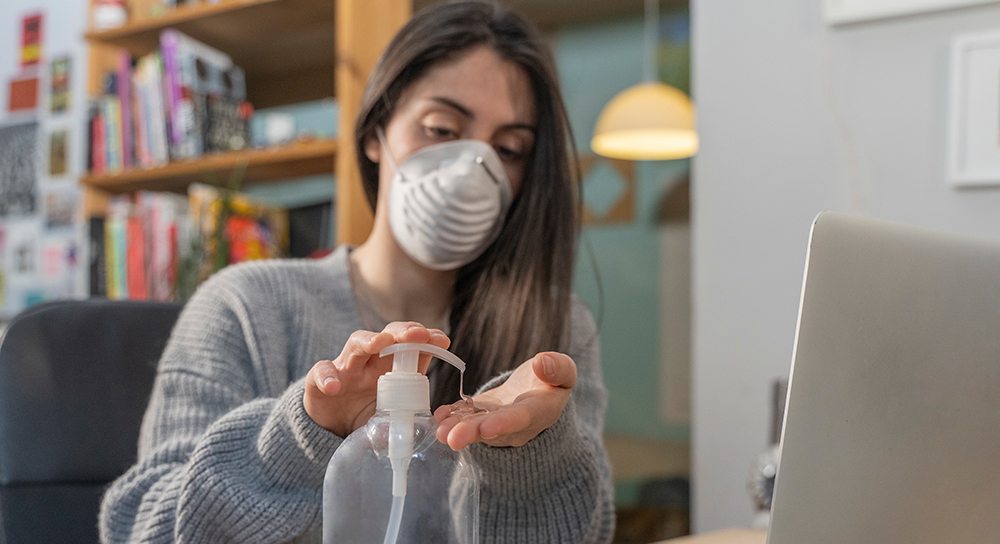 A woman with a mask on using hand sanitizer.